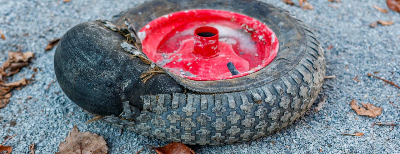A damaged wheel from a construction truck and a broken tire from a swollen hernia on a tire lies on the dirt side of the road