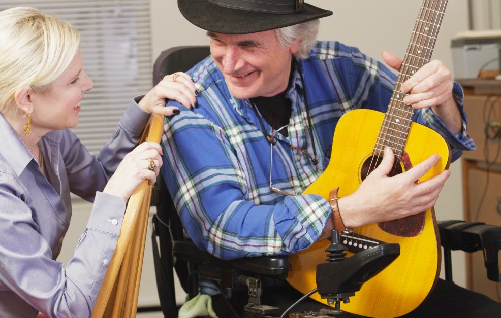 20 Dec 2012, Rockport, Massachusetts, USA --- Musician with Multiple Sclerosis in a motorized wheelchair with his guitar playing for a friend --- Image by © Mark Hunt/Huntstock/Corbis