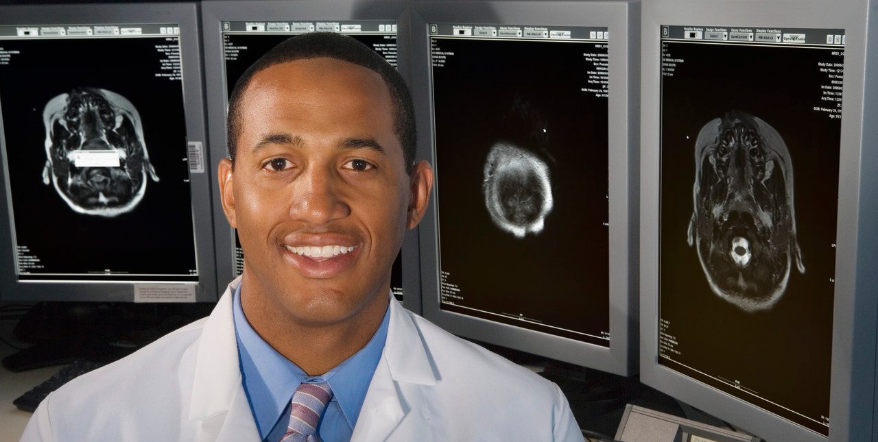 Detroit, Michigan, USA --- Man smiling in front of brain scans --- Image by © Paul Burns/Blend Images/Corbis