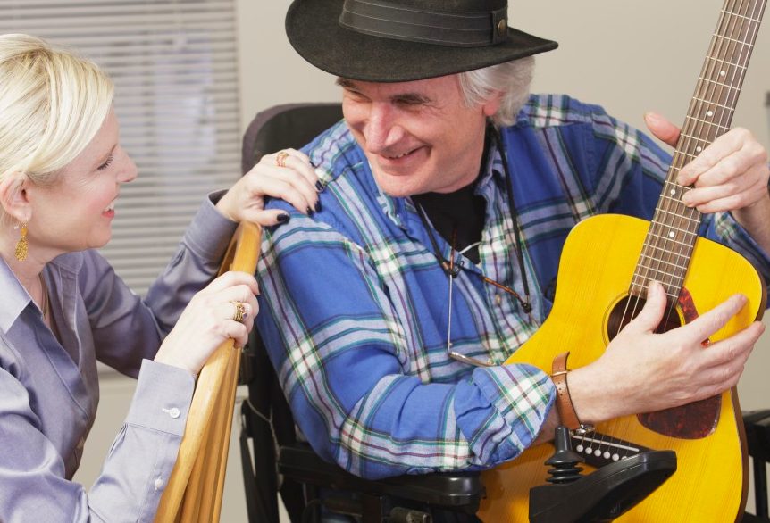 20 Dec 2012, Rockport, Massachusetts, USA --- Musician with Multiple Sclerosis in a motorized wheelchair with his guitar playing for a friend --- Image by © Mark Hunt/Huntstock/Corbis