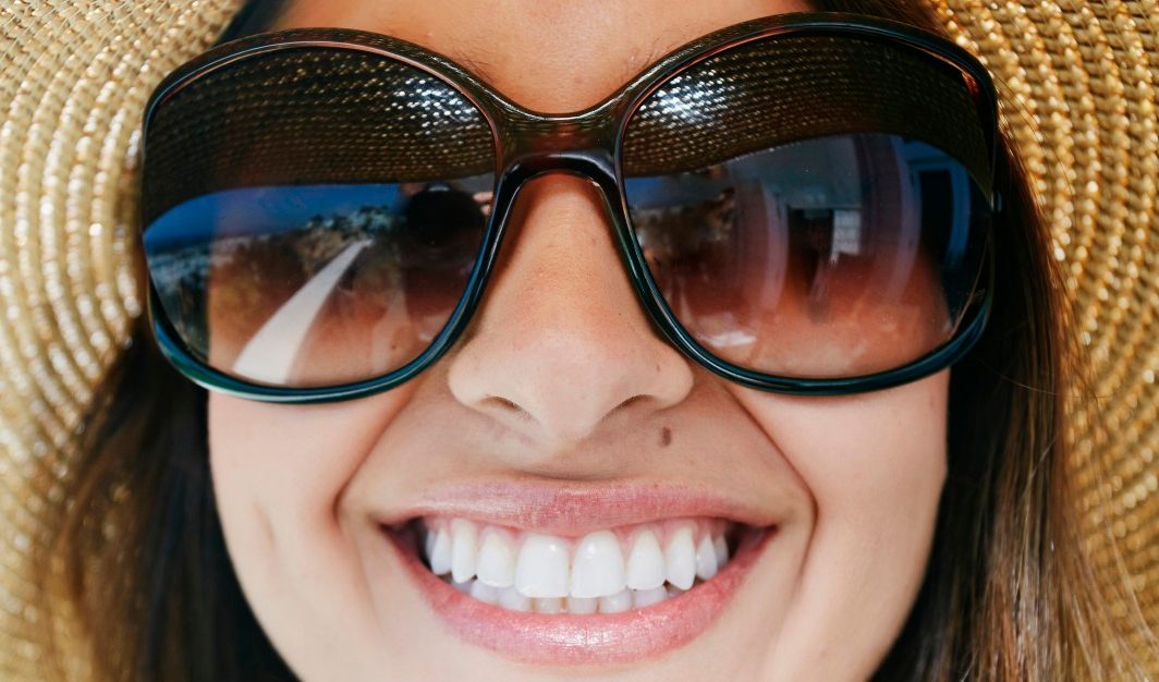 17 May 2014, Newport Beach, California, USA --- Smiling mixed race woman wearing sunglasses and sun hat --- Image by © Blend Images/Corbis