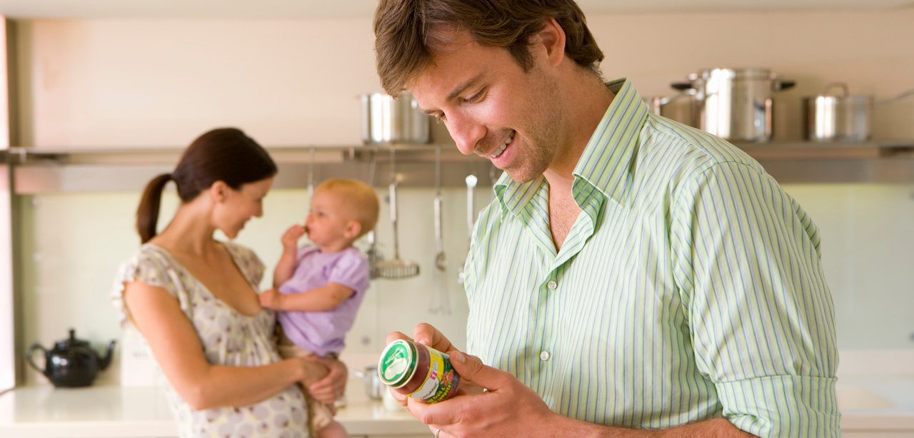 Young couple in kitchen, pregnant woman with baby girl (6-9 months), man looking at baby food label --- Image by © Juice Images/Corbis