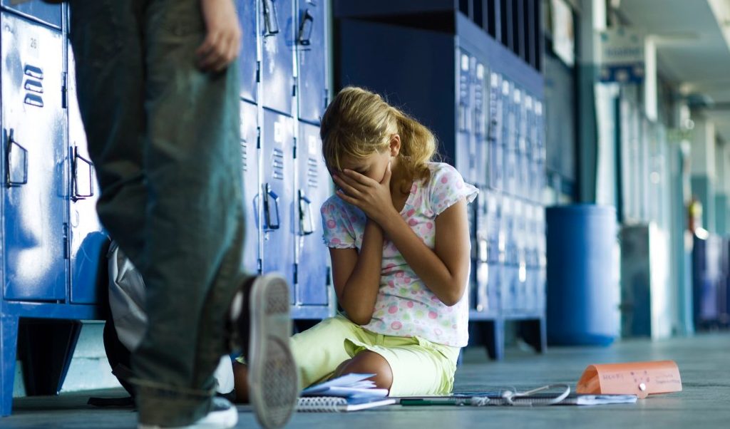 Female junior high student sitting on floor holding head in hands, boy standing smugly nearby --- Image by © Frederic Cirou/PhotoAlto/Corbis