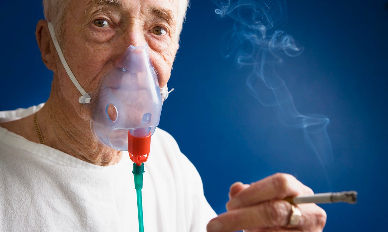 Elderly Patient Wearing Oxygen Mask and Smoking Cigarette --- Image by © Roy McMahon/Corbis