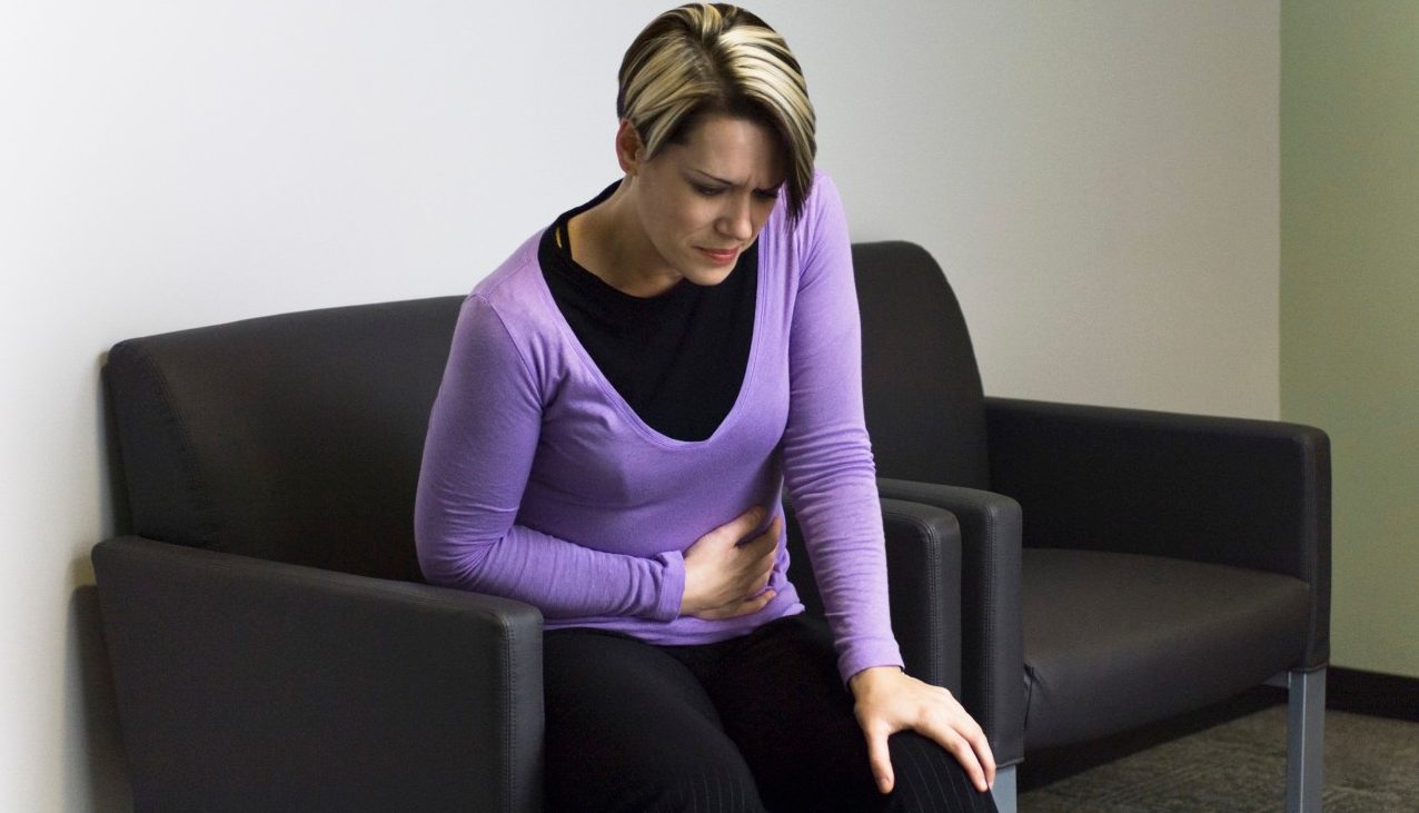 Woman sitting in hospital waiting room holding stomach --- Image by © Michele Constantini/PhotoAlto/Corbis