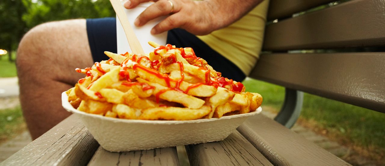 Overweight Man on Bench Next to French Fries --- Image by © Peter Reali/Corbis