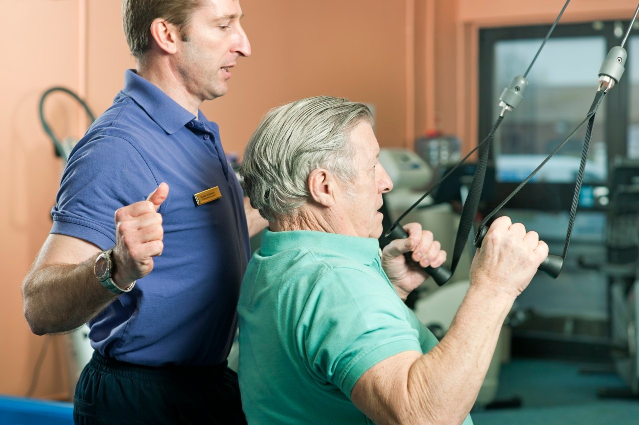 Trainer helping older man exercise --- Image by © Colin Hawkins/cultura/Corbis