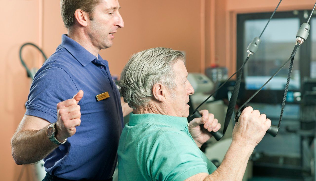 Trainer helping older man exercise --- Image by © Colin Hawkins/cultura/Corbis