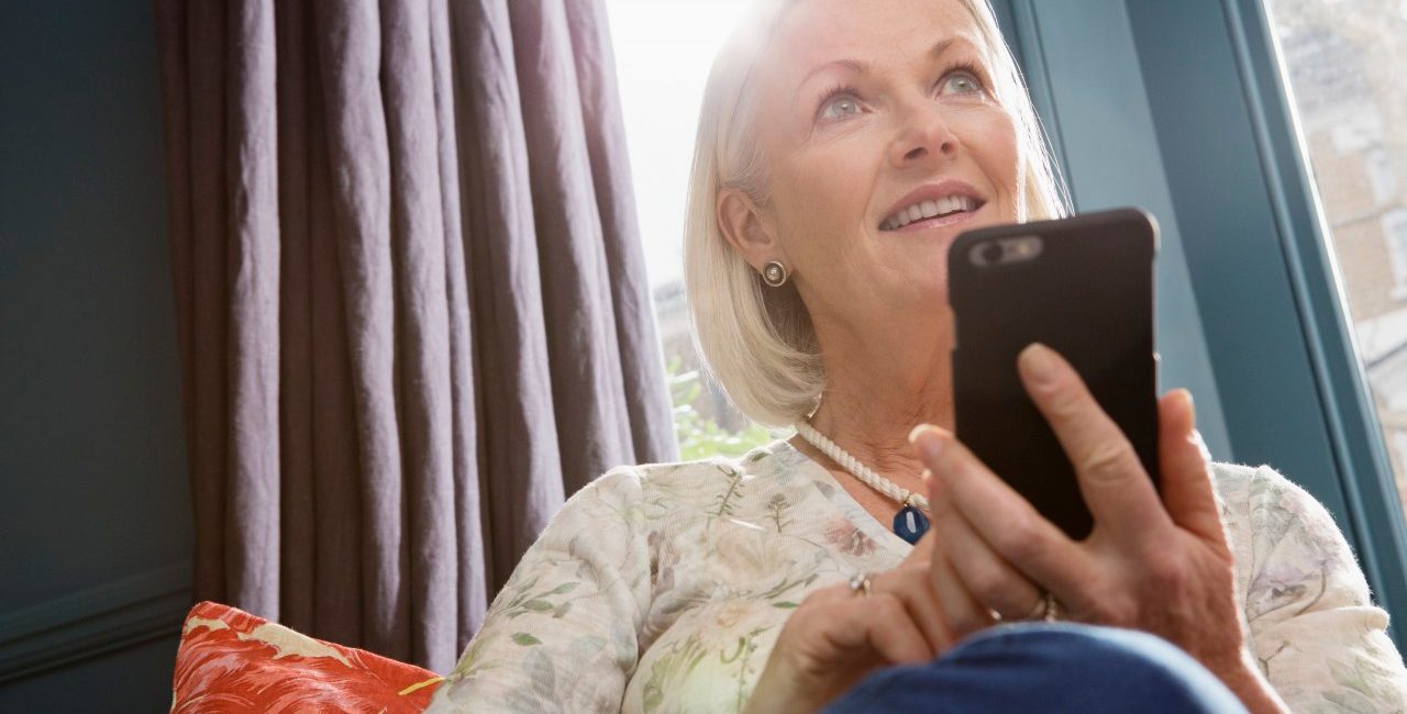 Woman sitting on sofa using smartphone --- Image by © Corbis