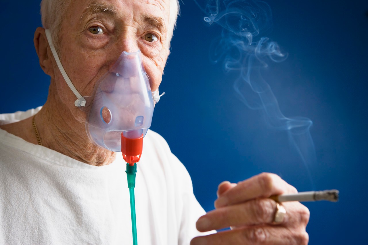 Elderly Patient Wearing Oxygen Mask and Smoking Cigarette --- Image by © Roy McMahon/Corbis