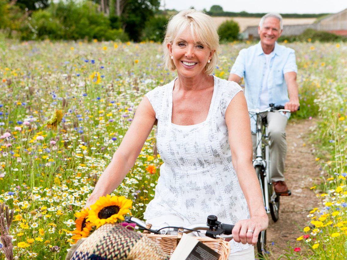 Smiling senior couple riding bicycles on path through field of wildflowers --- Image by © Juice Images/Corbis