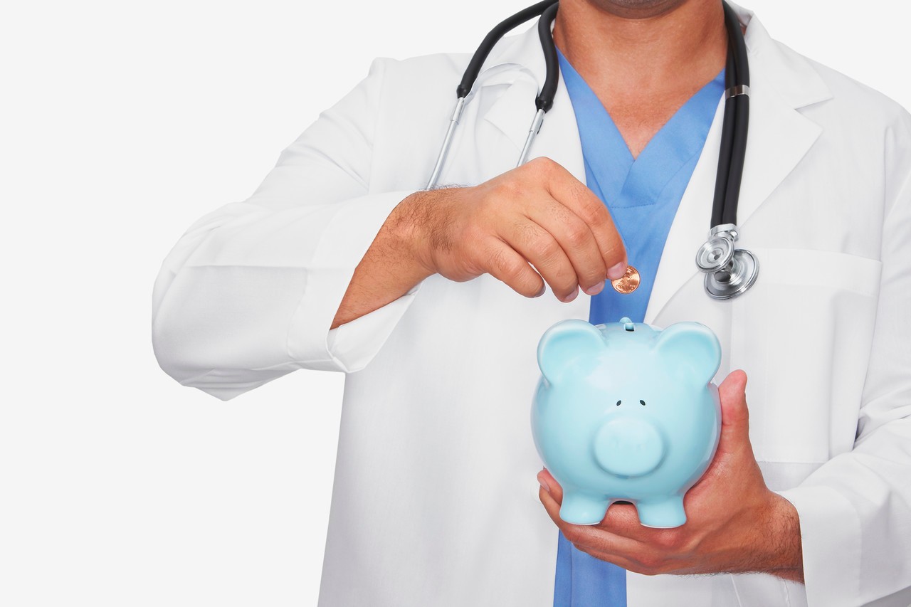 Mid section view of a male doctor inserting a coin into a piggy bank --- Image by © Hola Images/Corbis