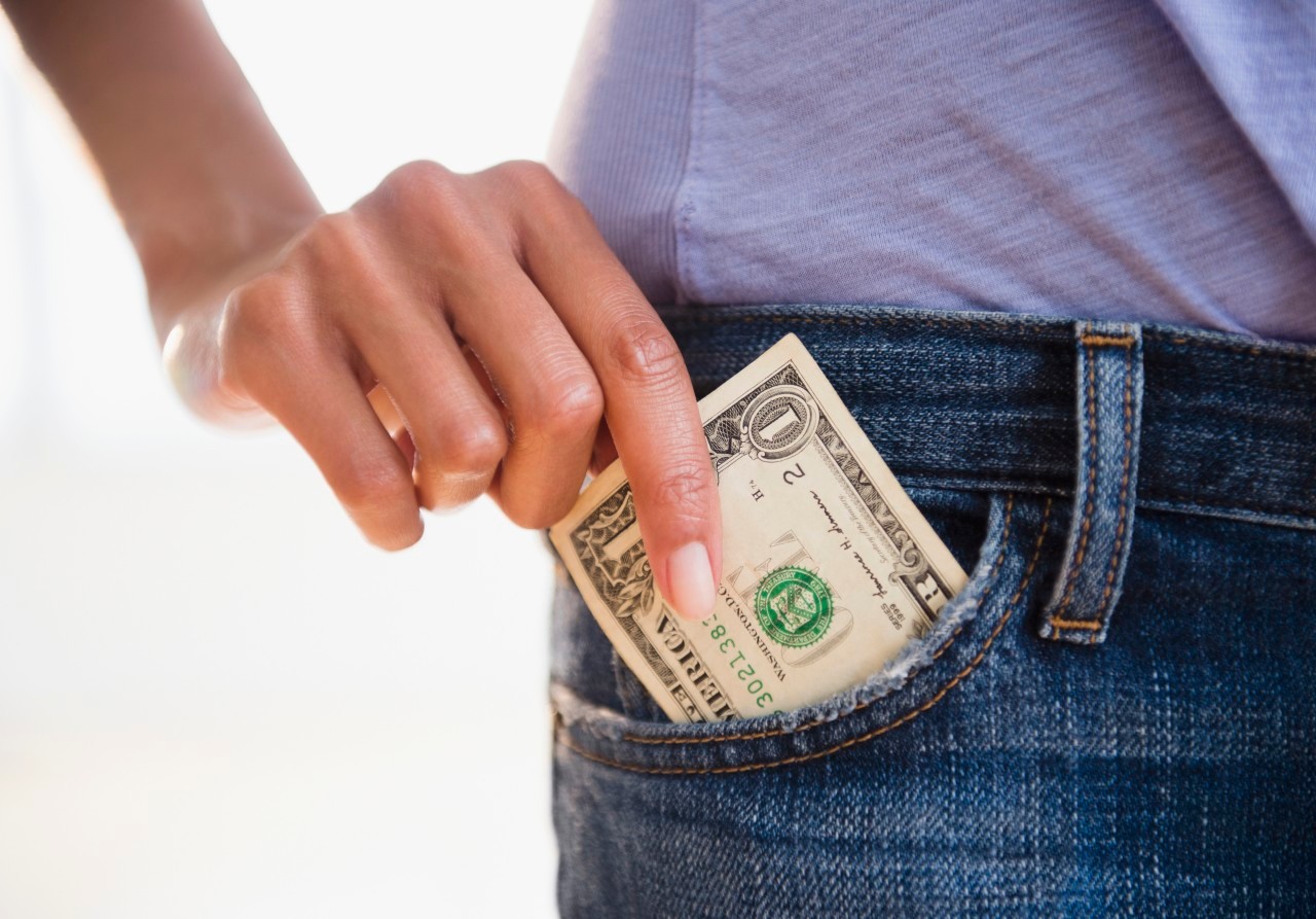 Cape Verdean woman taking dollar bill from pocket --- Image by © JGI/Jamie Grill/Blend Images/Corbis