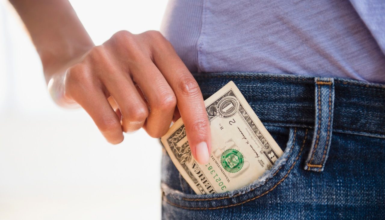 Cape Verdean woman taking dollar bill from pocket --- Image by © JGI/Jamie Grill/Blend Images/Corbis