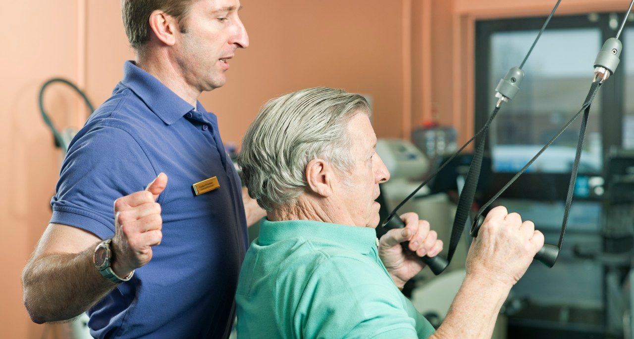 Trainer helping older man exercise --- Image by © Colin Hawkins/cultura/Corbis