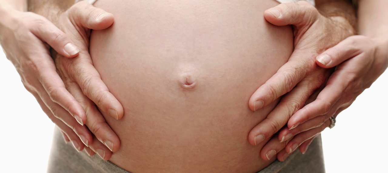 F002/6291 Expectant parents. Pregnant woman and her partner resting their hands on her swollen abdomen. She is in her third trimester. --- Image by © Ian Hooton/Science Photo Library/Corbis