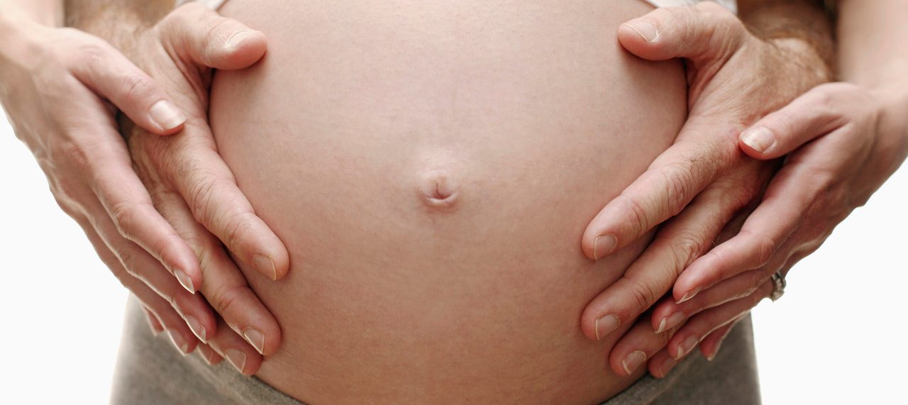 Expectant parents. Pregnant woman and her partner resting their hands on her swollen abdomen. She is in her third trimester. --- Image by © Ian Hooton/Science Photo Library/Corbis