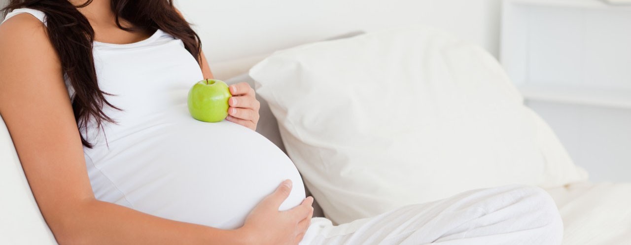 42-54192571 Attractive pregnant woman holding an apple on her belly while ly --- Image by © Wavebreak Media Ltd/Veer/Corbis