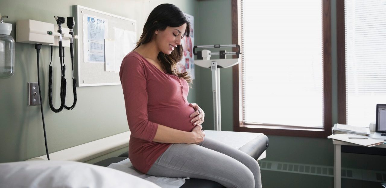 0042-11-30T00:00:00.000Z 10 Dec 2014 --- Smiling pregnant woman holding stomach in examination room --- Image by © Hero Images Inc./Hero Images Inc./Corbis