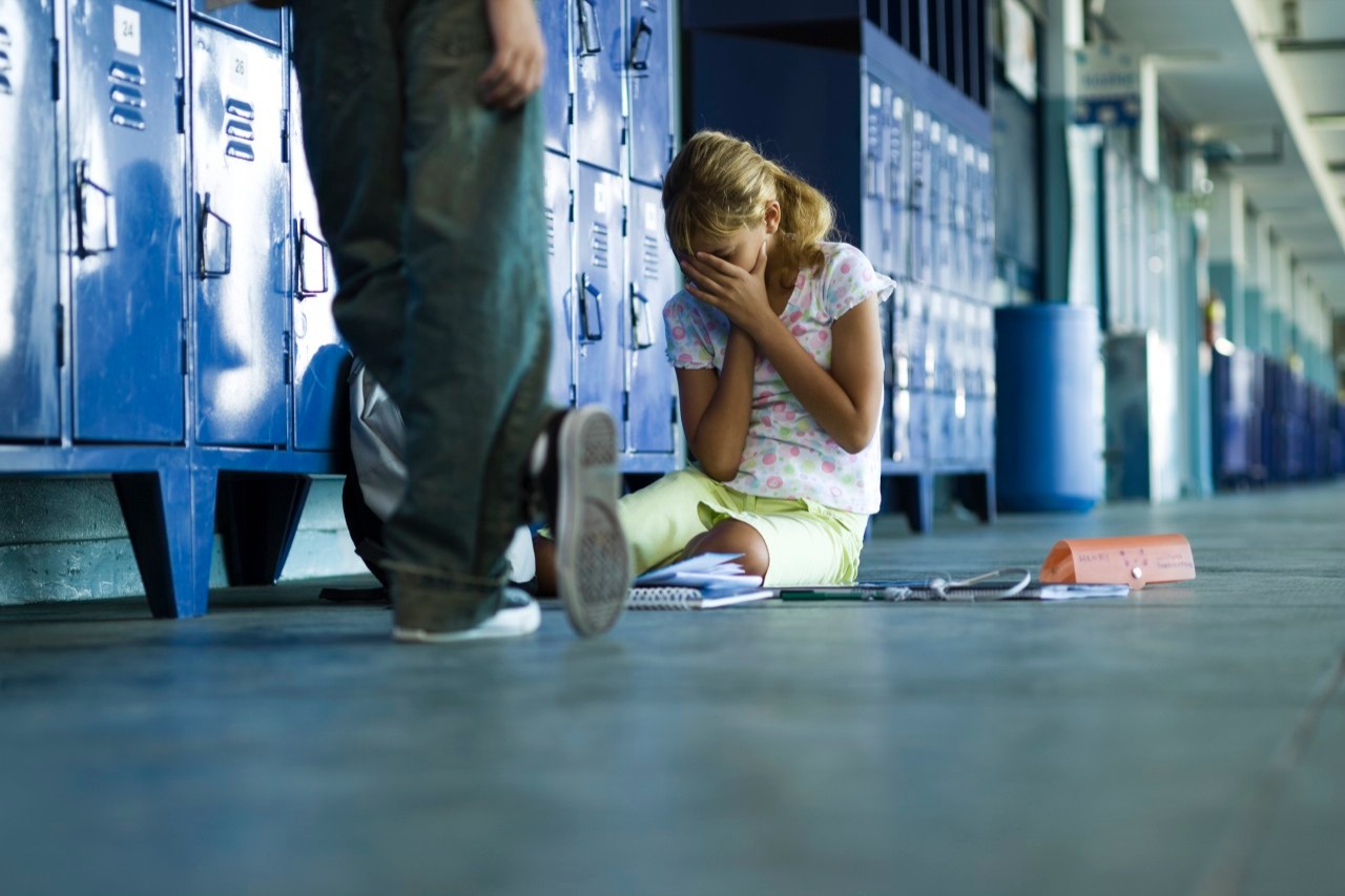 Female junior high student sitting on floor holding head in hands, boy standing smugly nearby --- Image by © Frederic Cirou/PhotoAlto/Corbis