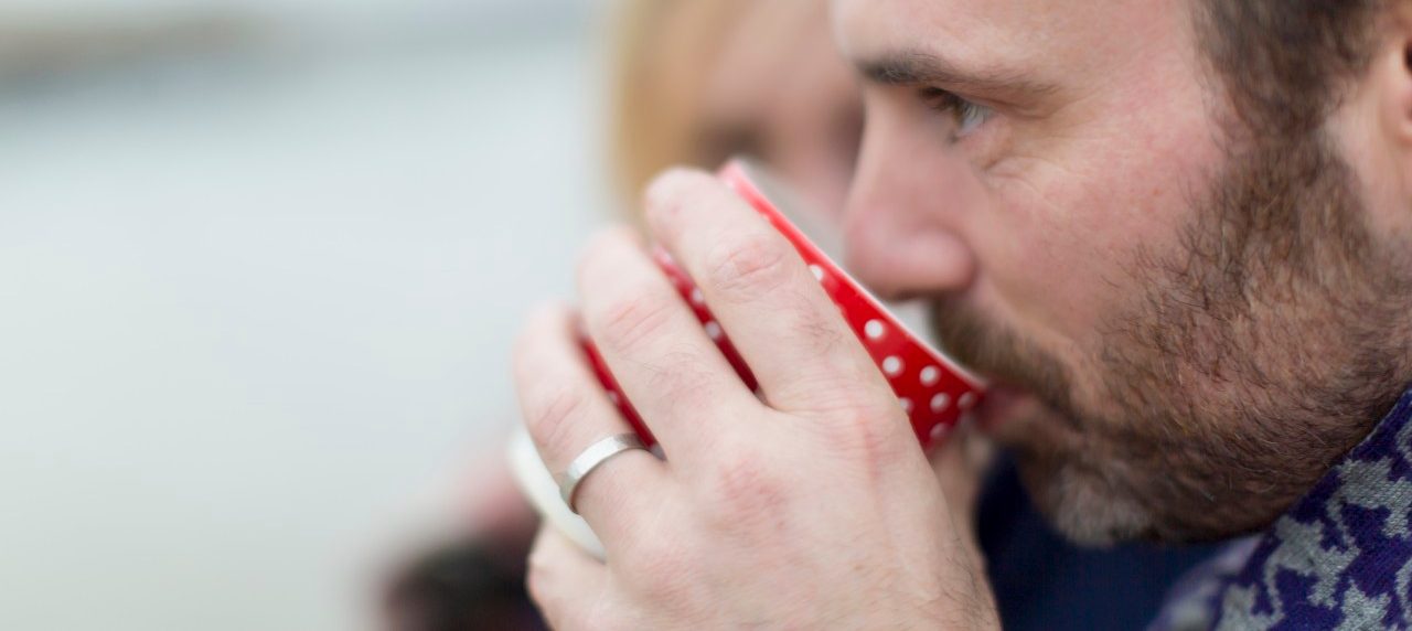 16 Nov 2014 --- Couple on beach, man drinking hot drink --- Image by © dotdotred/Corbis