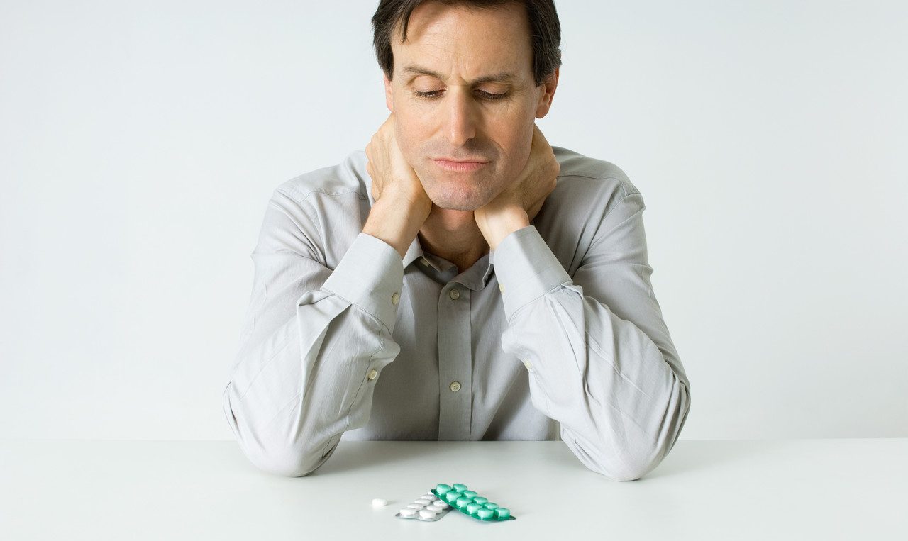 Man Sitting Next To Pills, Holding Neck, Looking Down --- Image by © Michele Constantini/PhotoAlto/Corbis