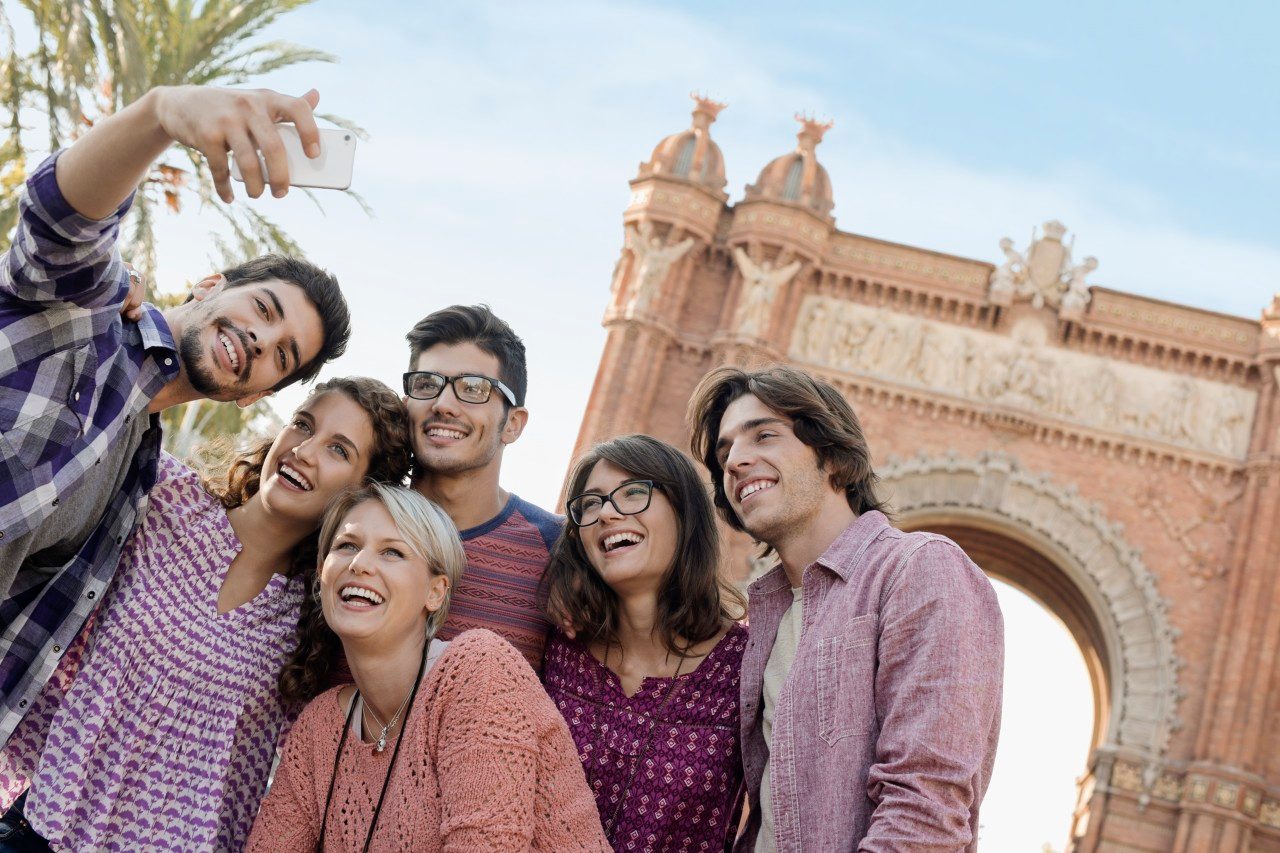 Barcelona, Spain --- Group of friends taking selfie in front of arch, Barcelona, Catalonia, Spain --- Image by © Hiya Images/Corbis