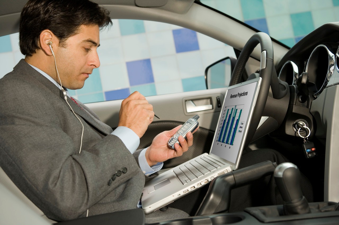 Businessman using his laptop computer and PDA in his car --- Image by © Steve Hix/Somos Images/Corbis