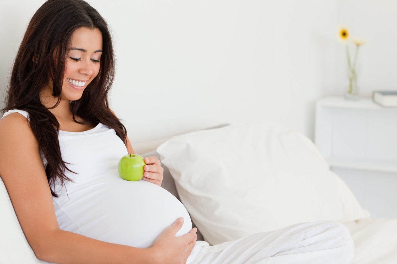 Attractive pregnant woman holding an apple on her belly while ly --- Image by © Wavebreak Media Ltd/Veer/Corbis