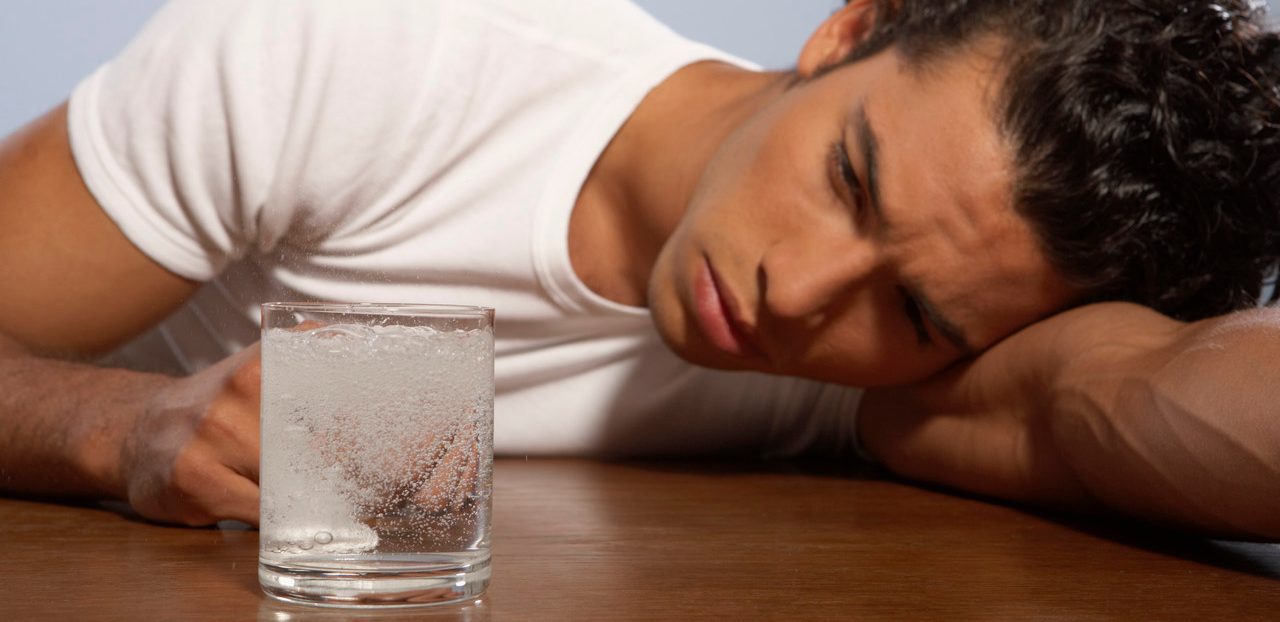 Young Man Lying Beside a Glass of Water with a Tablet on Table --- Image by © Turbo/Corbis