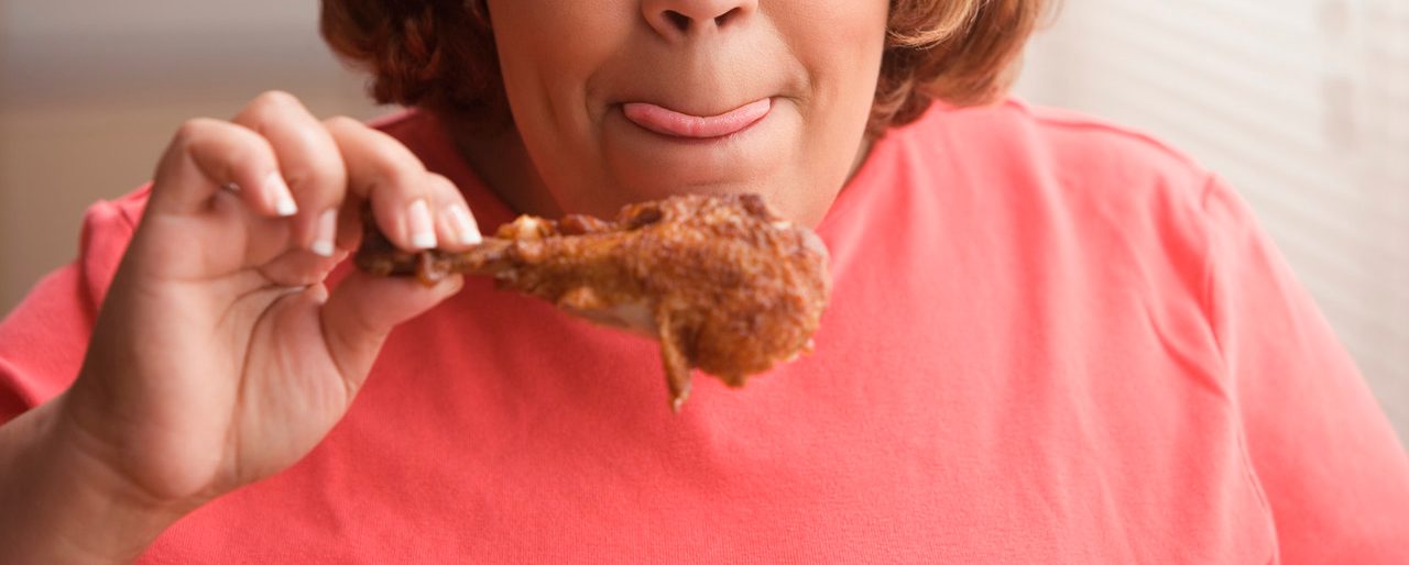 Middle-aged overweight Hispanic woman licking her lips and looking at a piece of fried chicken --- Image by © Jose Luis Pelaez, Inc./Blend Images/Corbis