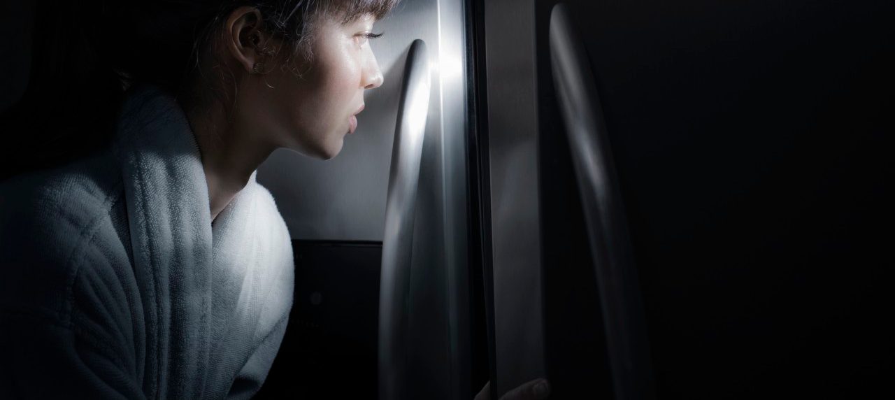 Mixed race woman peering into refrigerator at night --- Image by © Jill Giardino/Blend Images/Corbis