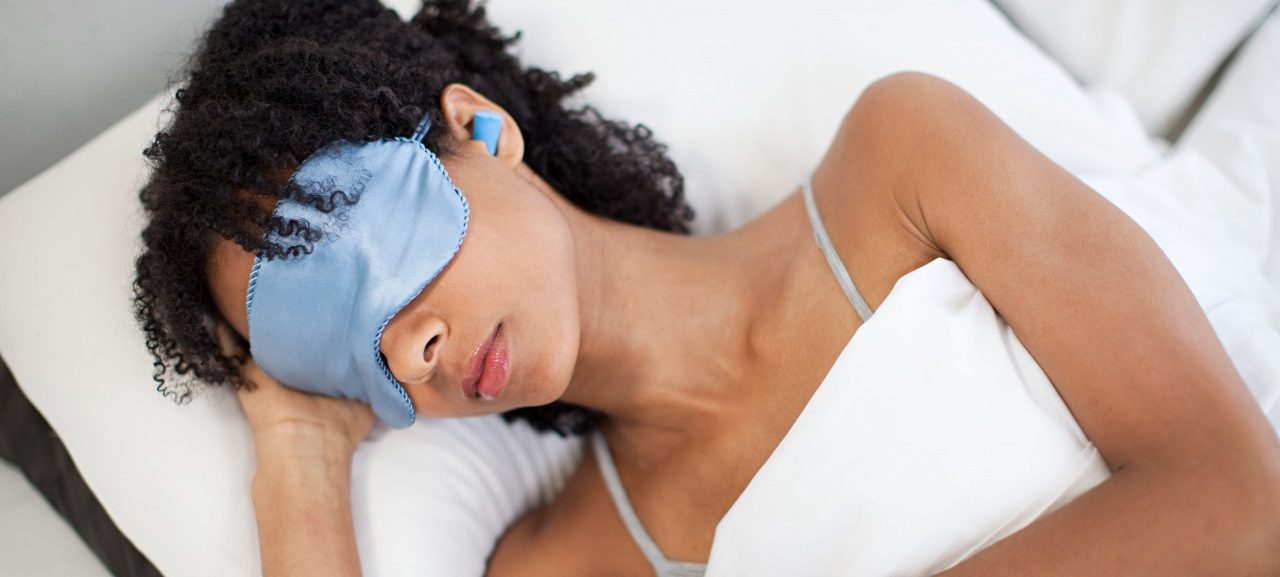 Woman sleeping in eye mask and ear plugs --- Image by © Image Source/Corbis