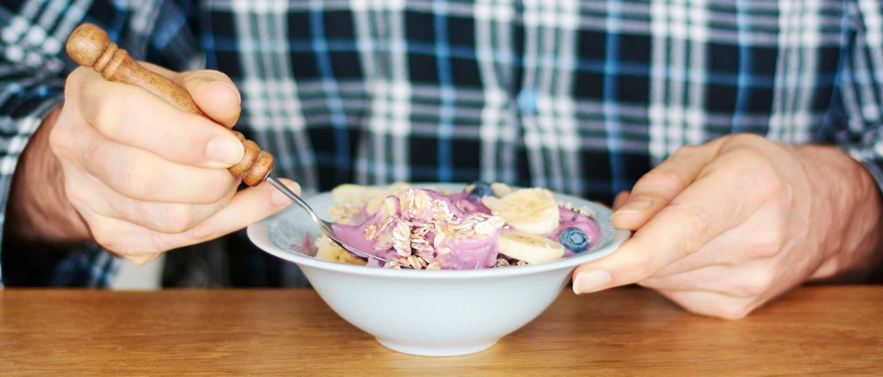 42-66634734 21 Dec 2014 --- Man in pajamas eating granola with soy yogurt, blueberries and banana --- Image by © Harald Walker/Westend61/Corbis