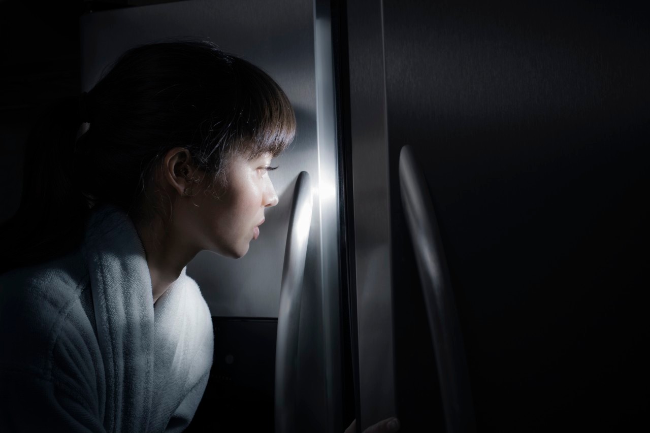 Mixed race woman peering into refrigerator at night --- Image by © Jill Giardino/Blend Images/Corbis