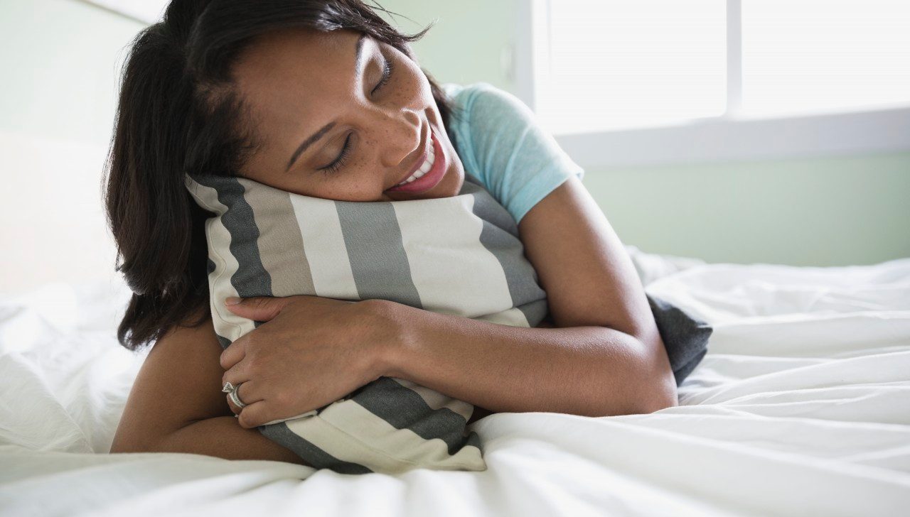 15 May 2013 --- Woman holding pillow while lying on bed. --- Image by © Hero Images/Corbis