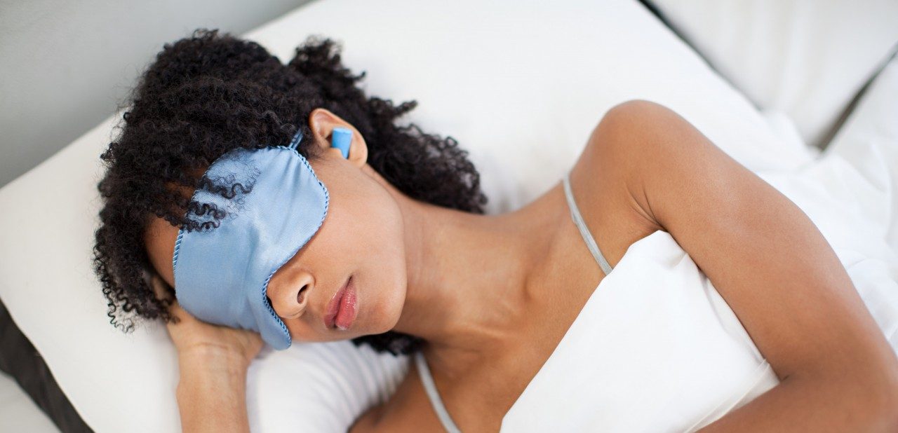Woman sleeping in eye mask and ear plugs --- Image by © Image Source/Corbis