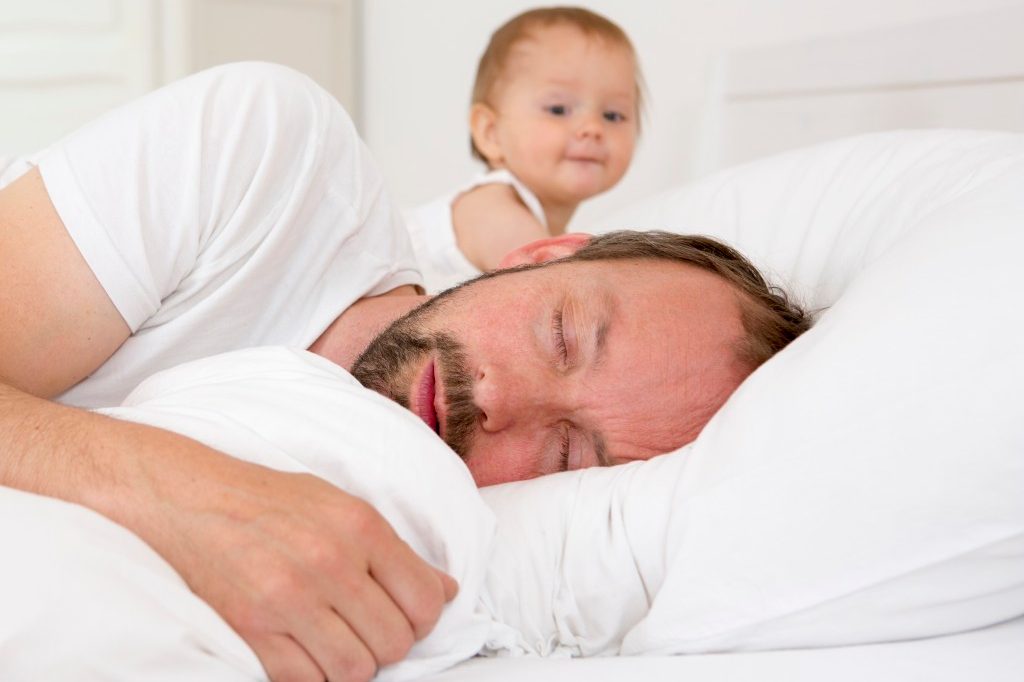 13 Jul 2014 --- Father asleep in bed, baby daughter watching --- Image by © Judith Haeusler/Corbis