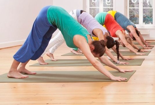 Group of mid adult women and mid adult man doing downward-facing dog pose in yoga studio --- Image by © Mareen Fischinger/Corbis